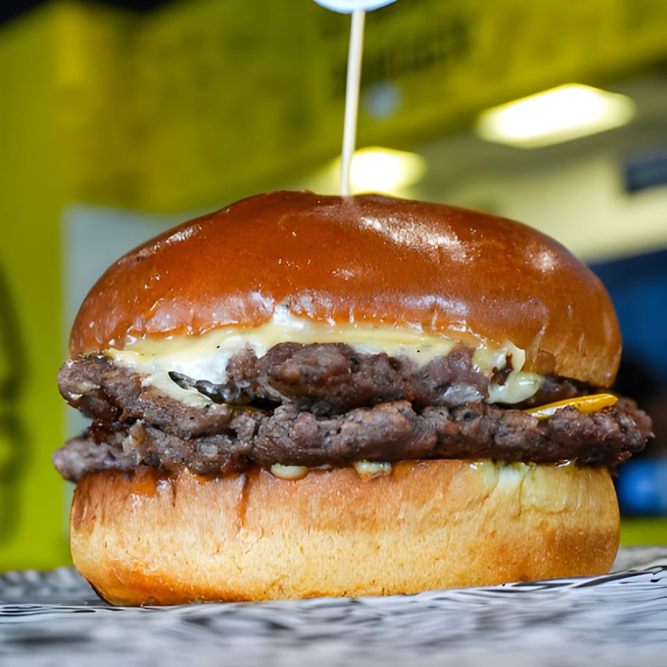 A double patty STUDENT BURGER with melted cheese and a shiny bun, served on crinkled paper.