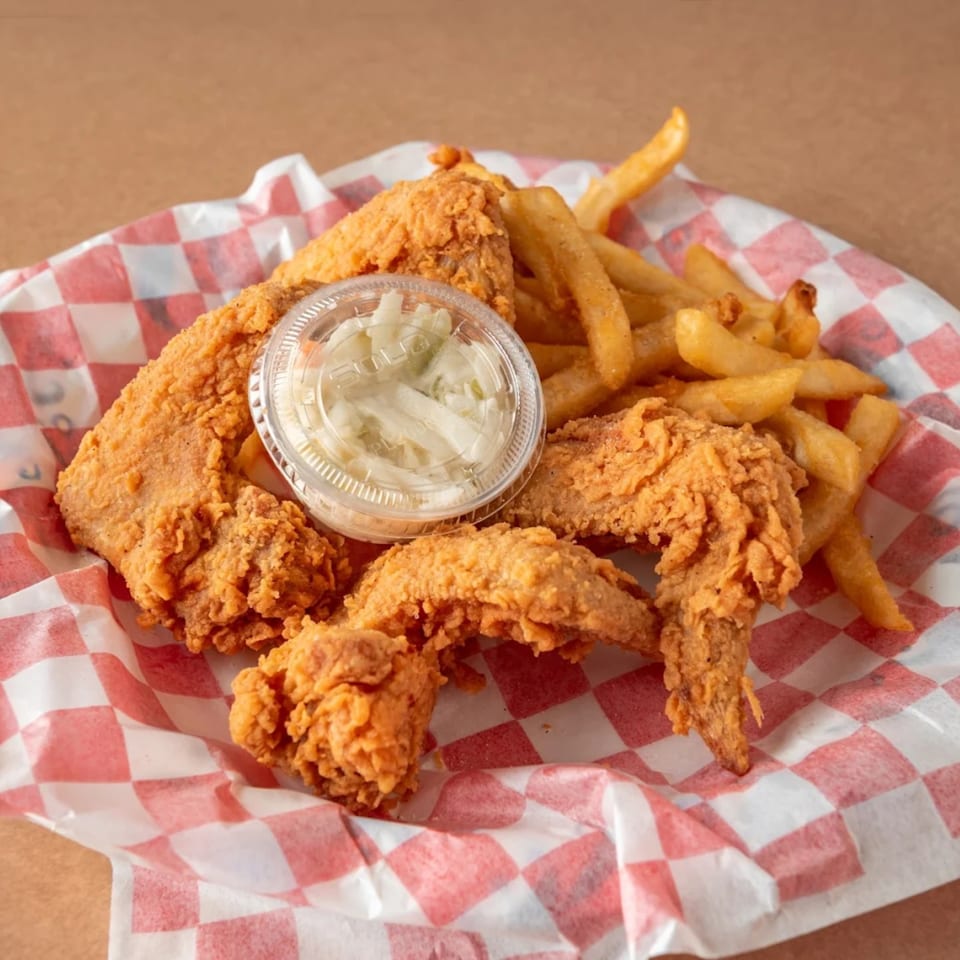 Crispy fried chicken wings and golden french fries with a side of coleslaw in a red and white checkered basket.