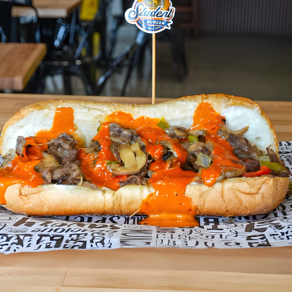 A Student Burger cheesesteak sandwich with steak, mushrooms, peppers, onions, and orange sauce.