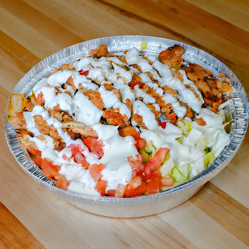 Chicken and rice platter with white sauce, diced tomatoes, and lettuce in a foil container.